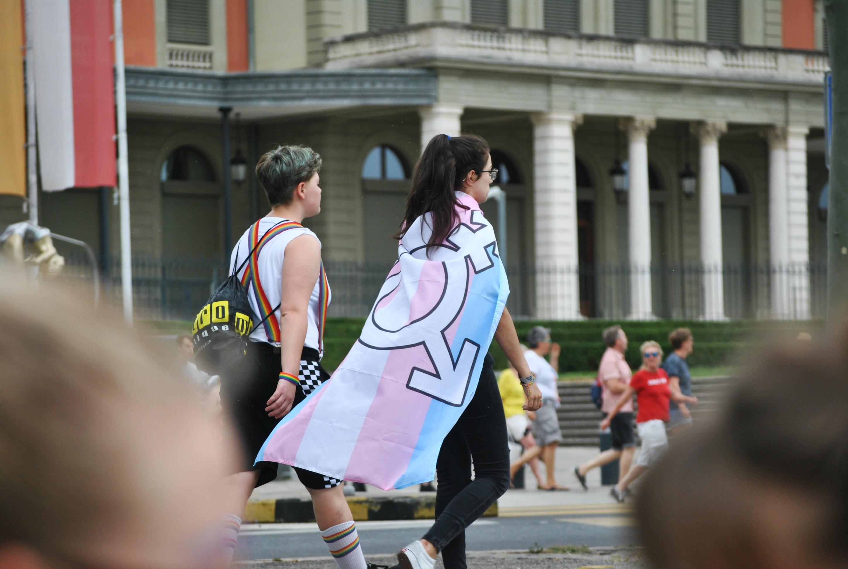 Deux personnes qui marchent, l'une portant le drapeau de la fierté trans.