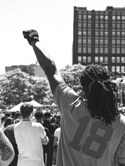 Seen from behind, a person at a rally holds a fist in the air. 