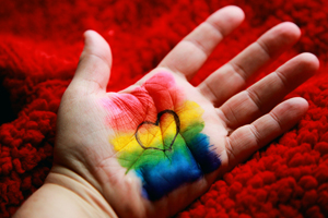 An open palm has a rainbow painted across it, with a small heart inside the raindow