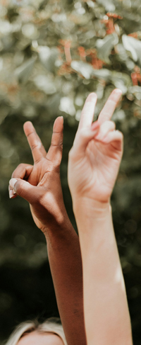 Two arms – one Black, one white – make peace signs against a backdrop of green trees 
