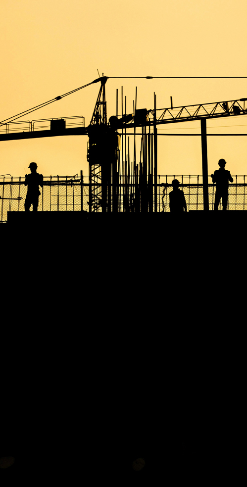 Des &eacute;quipements de chantier et des travailleurs portant un casque de s&eacute;curit&eacute; apparaissent en silhouette sur fond de ciel orang&eacute; spectaculaire