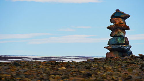 A brown inukshuk stands near a rocky coastline in daytime