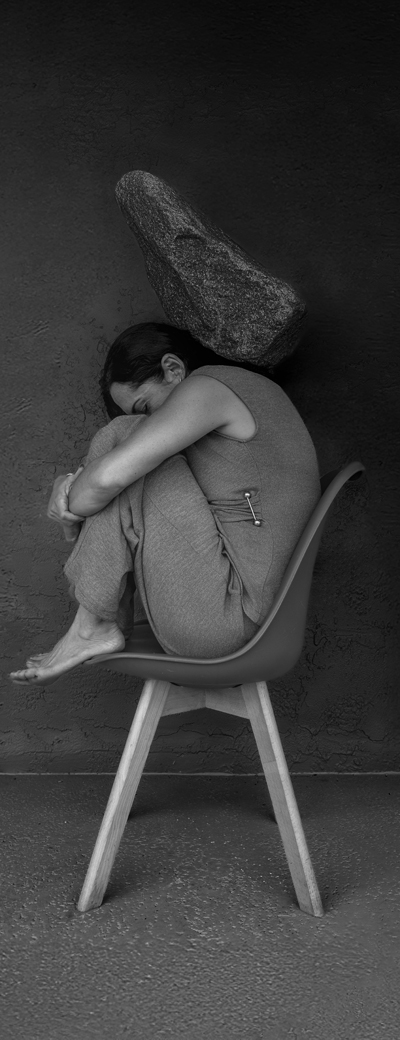 Photo en noir et blanc d&rsquo;une femme assise sur un tabouret, les bras autour des jambes.